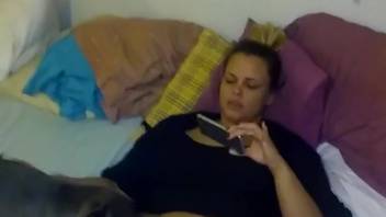 Excited woman touches herself on webcam with the dog nestled between her thighs